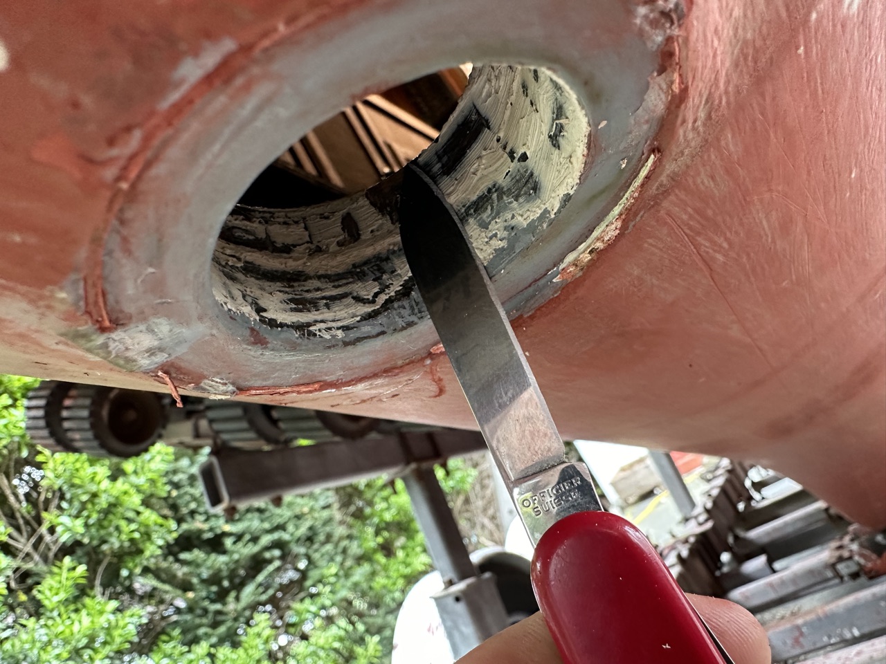 Cleaning old bedding compound from the thruhull opening with a knife, seen from the hull exterior
