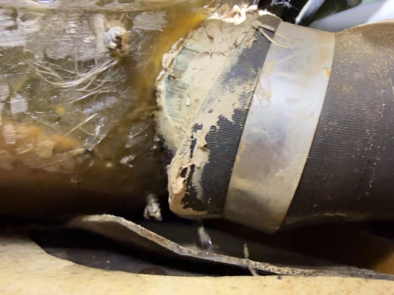 Close-up of the deteriorated original scupper hose where it meets the hull fitting, showing cracked compound and failed connection