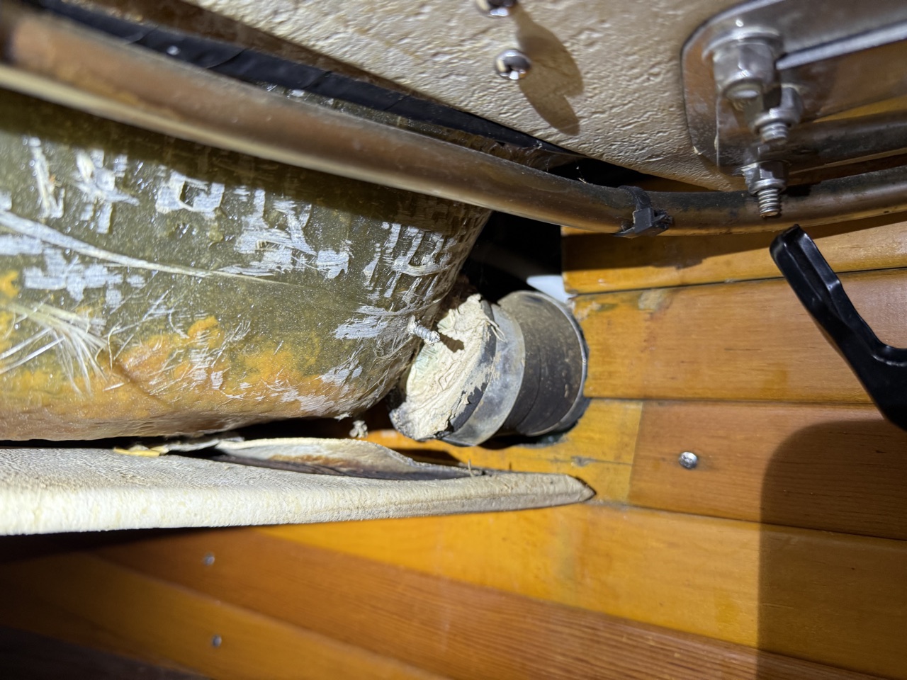 Interior view of the original foredeck scupper fitting from below deck, showing the original hose routing