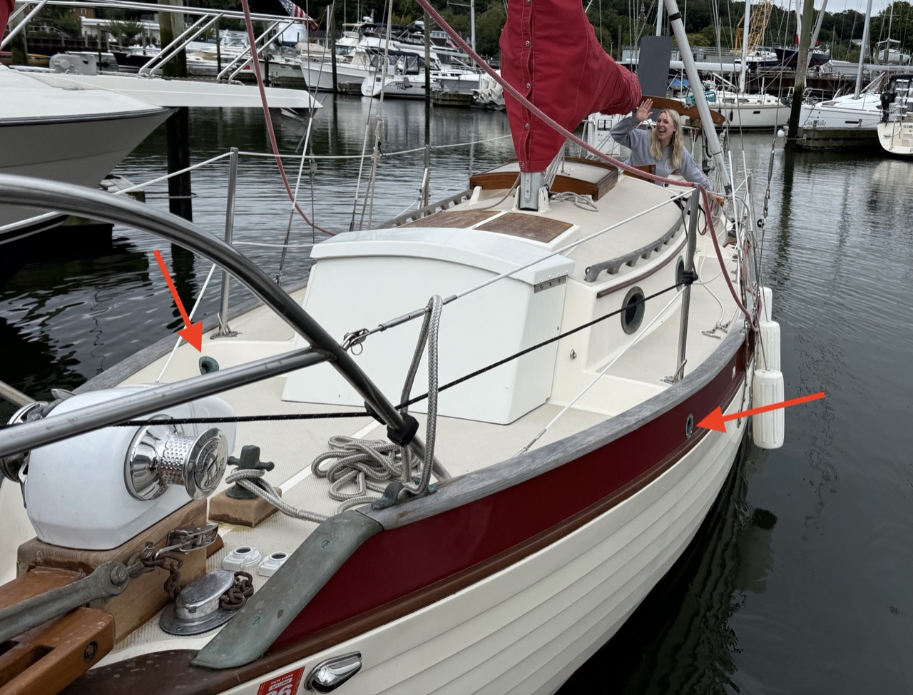 Queen of Hearts at the dock with red arrows pointing to the foredeck scupper locations on the hull