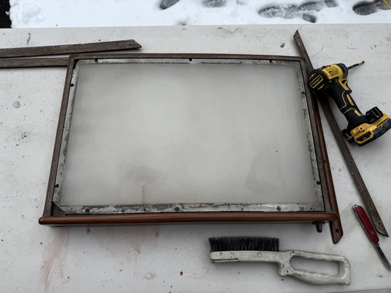 Aft cabin sliding hatch removed and laid on a table outside, showing grime and deteriorated sealant around the plastic panel