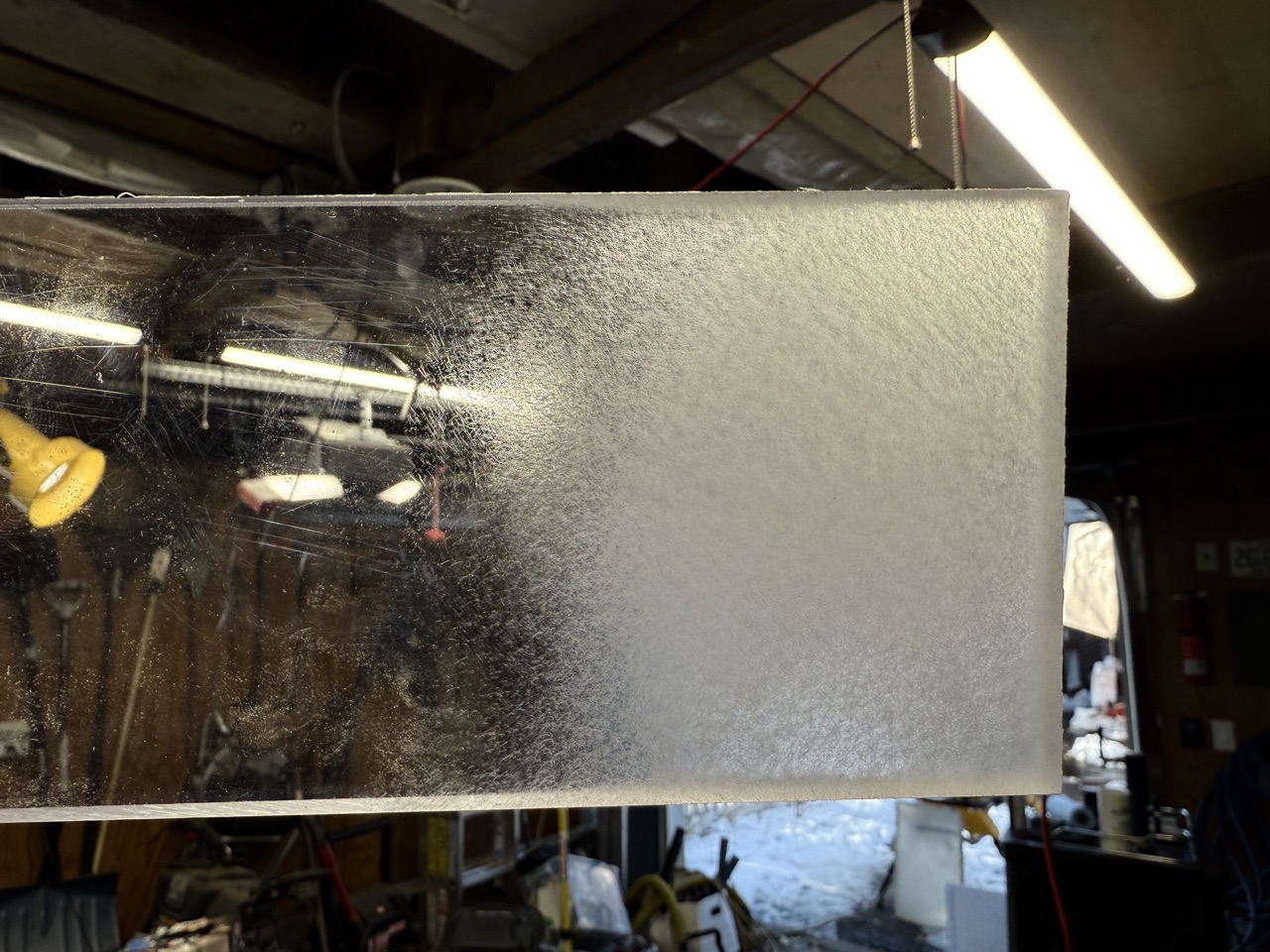 New polycarbonate sheet held up to the light showing the difference between the clear unsanded side and the frosted sanded side