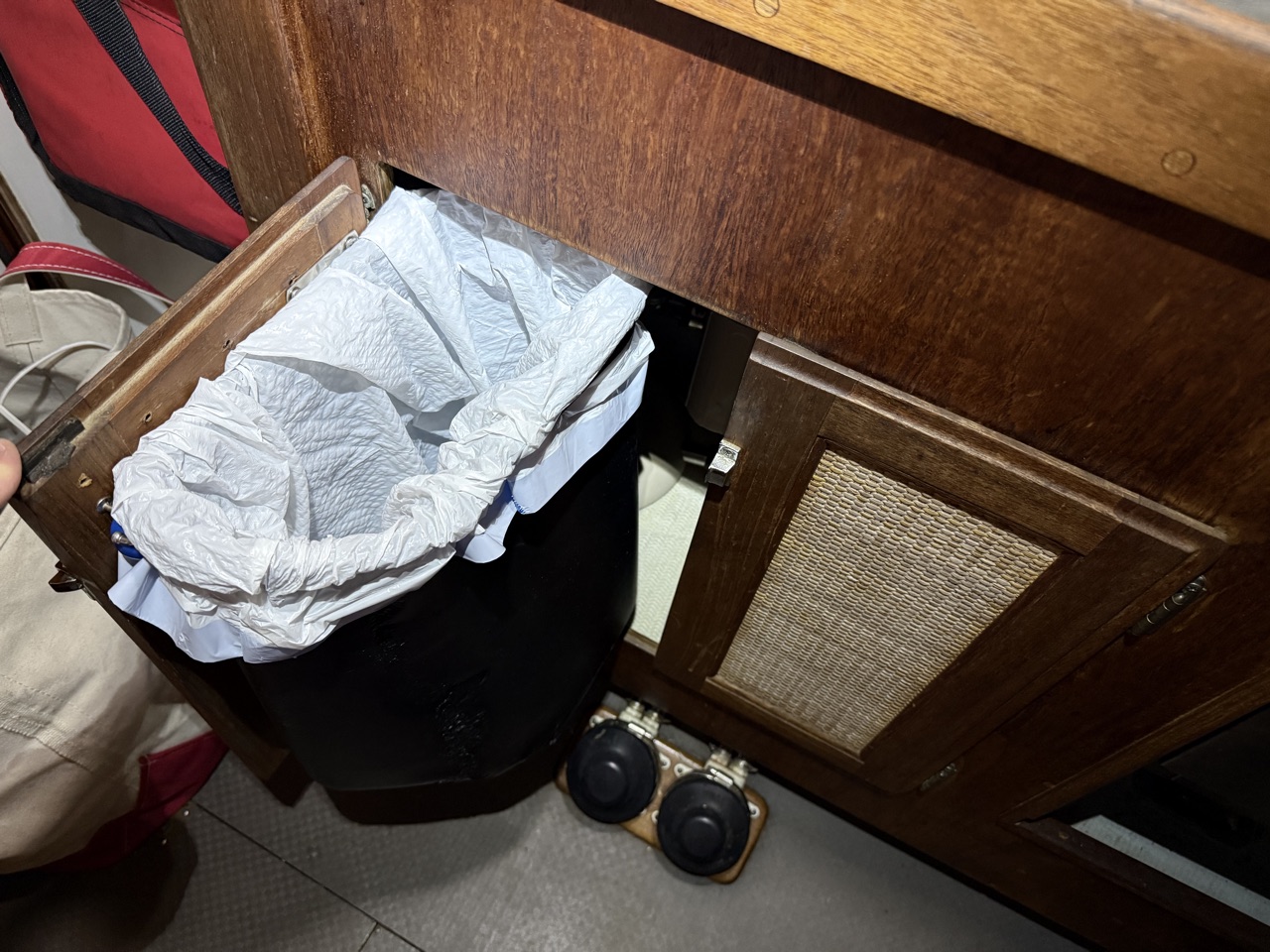 Modified trash can mounted inside the open under-sink cabinet door with a trash bag liner installed