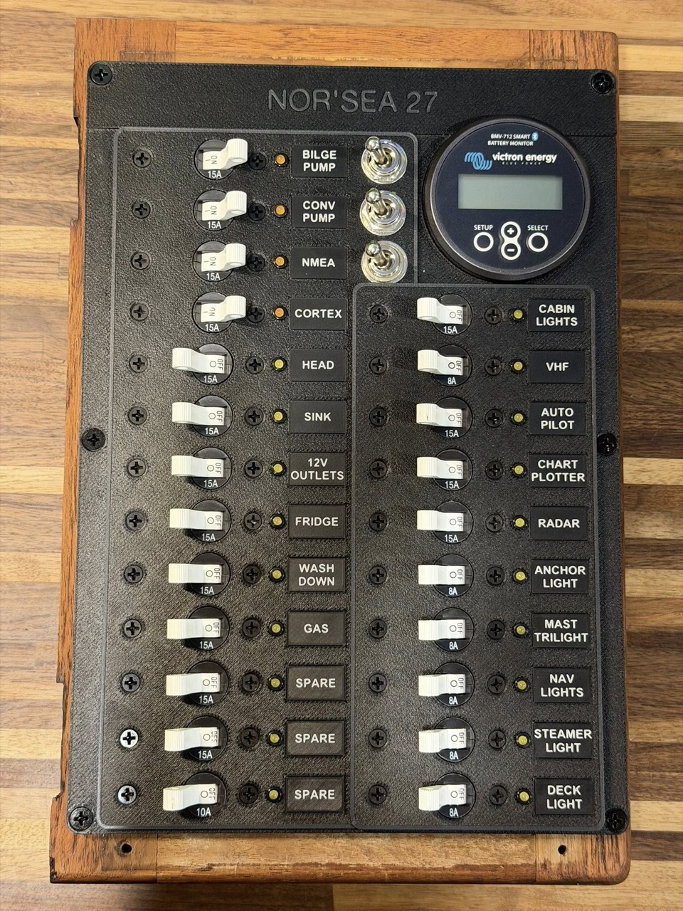 Assembled electrical panel on a workbench with all Blue Sea breakers, toggles, and Victron BMV-712 installed before mounting in the boat